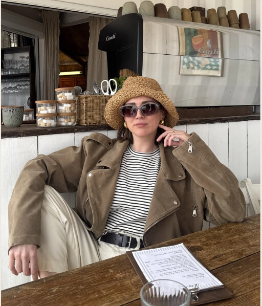 Manon attablée à un café, veste beige, chapeau de paille et lunettes de soleil